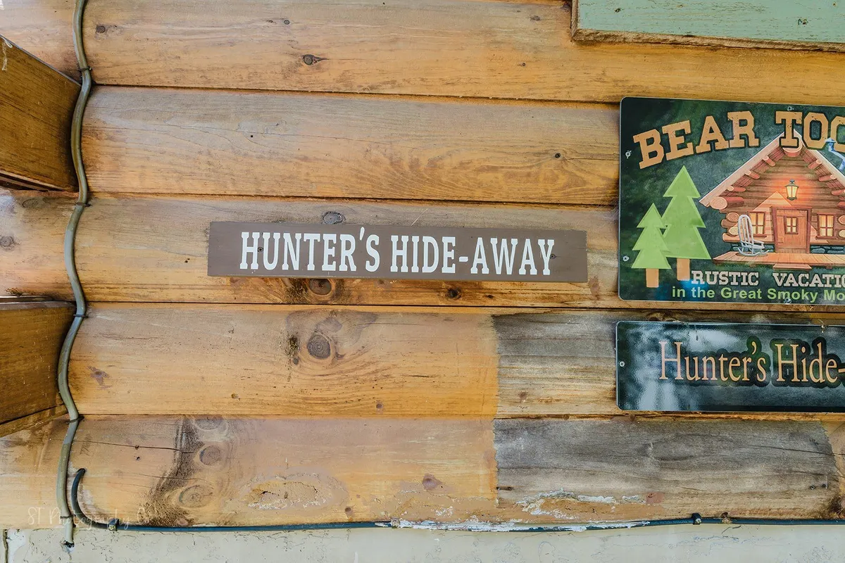 A rustic sign marks the entrance to Hunter's Hideaway, set against a backdrop of weathered wood and featuring a Bear Tooth sign, hinting at proximity to the Great Smoky Mountains and the adventure that awaits nearby.