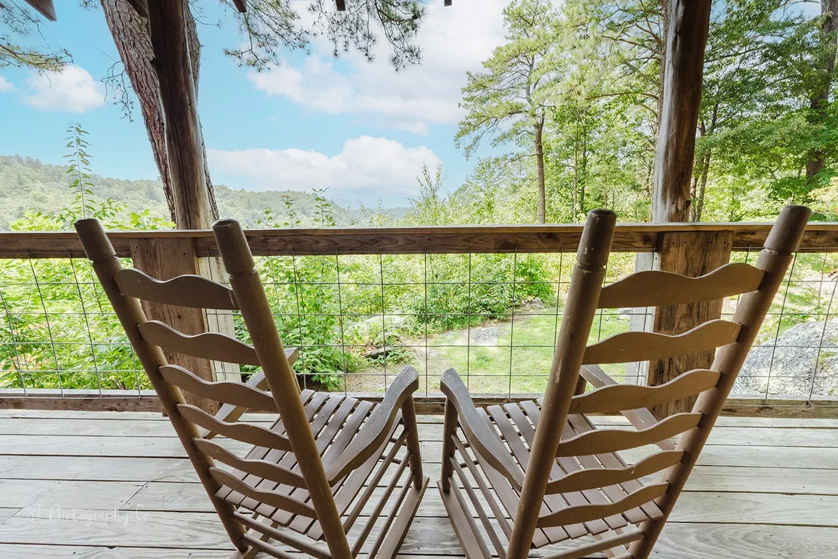 This exterior image features wooden rocking chairs overlooking lush greenery and distant hills, creating a sense of immersion in nature. The peaceful ambiance is perfect for relaxing with a pet after a day exploring nearby trails.