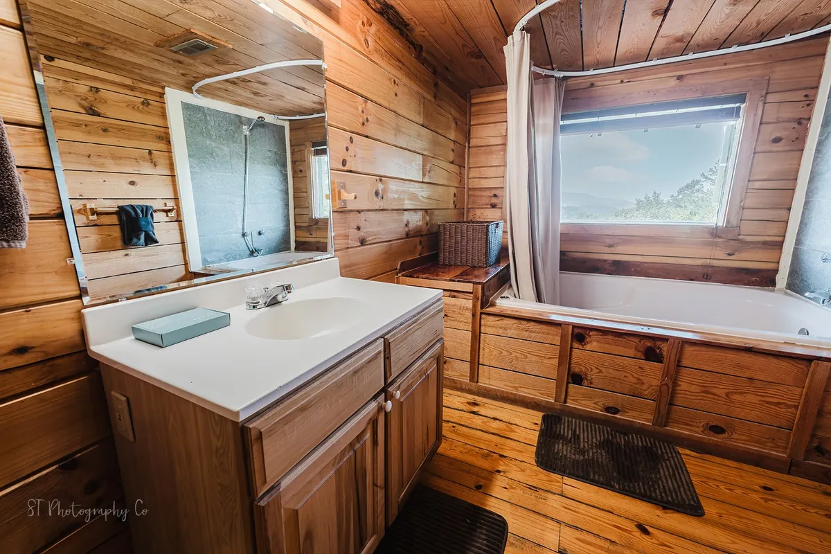 A serene bathroom with a bathtub positioned next to a large window, offering peaceful views of the outdoors. The wooden cabinetry and mirror contribute to a tranquil, private ambiance—perfect for relaxing soaks after a day of exploring.