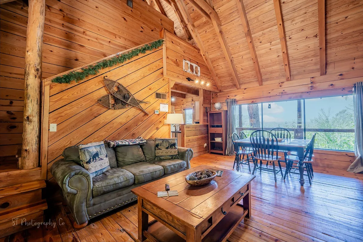 A bright living space with exposed wooden beams, a comfortable sofa, a dining table, and expansive windows that frame the mountain scenery outside. The area radiates warmth and invites guests to relax, socialize, or simply enjoy the tranquil views from indoors.