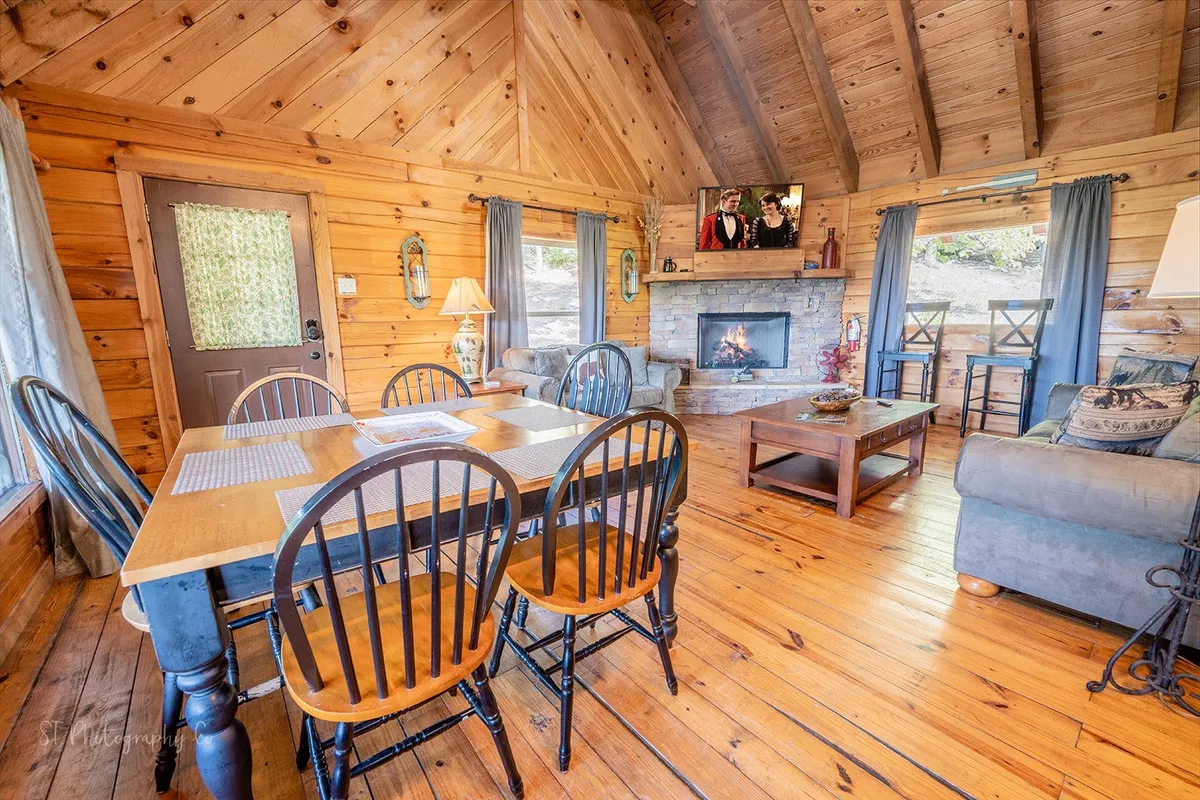 A warm, welcoming living area with a dining table set for a meal, a crackling fireplace, a comfortable sofa, and a television. The communal setup is ideal for sharing laughter, meals, and relaxing together after a day of adventure.