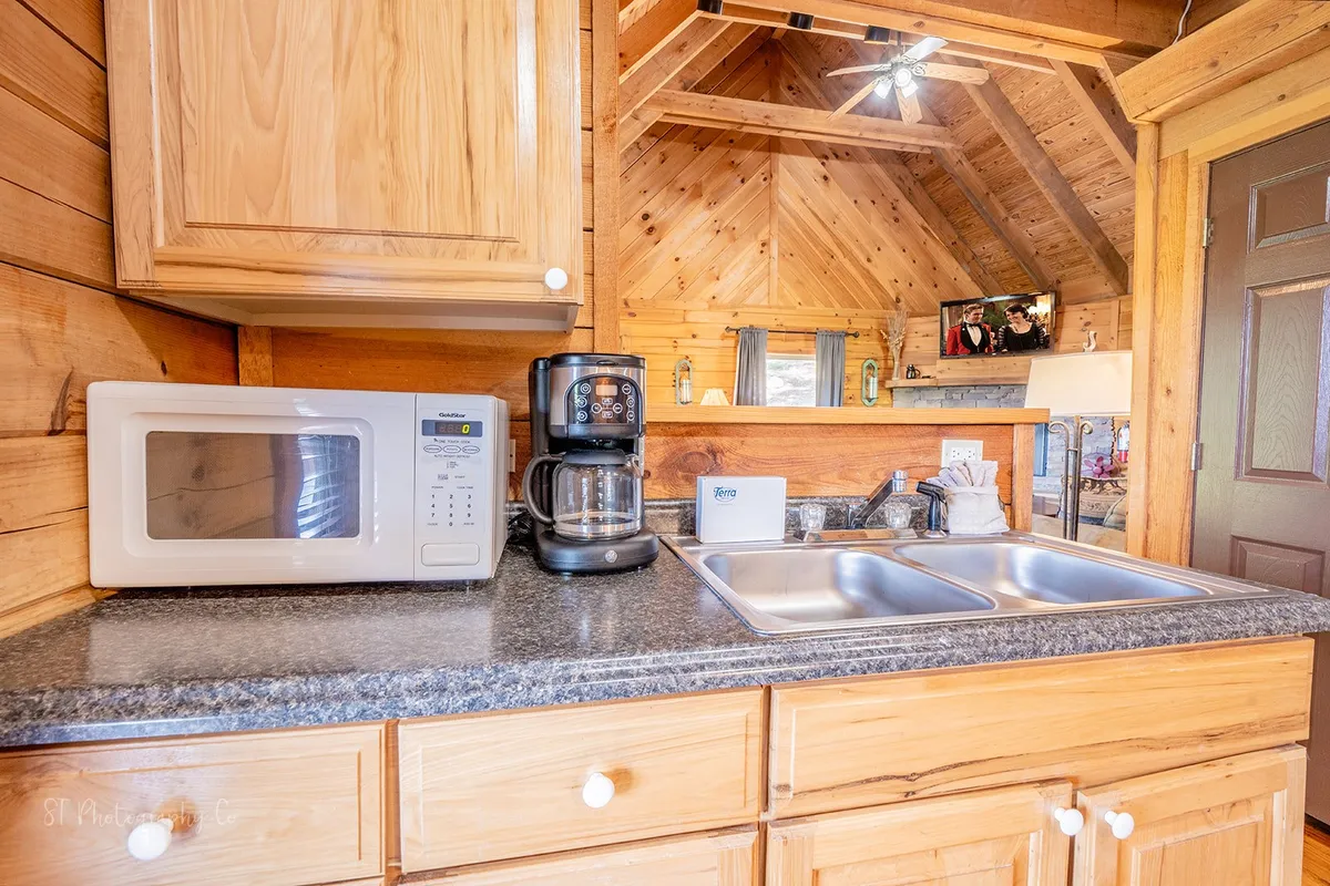 A cozy kitchen scene featuring a microwave, coffee maker, and wooden cabinets. The space is warm and homey, inviting guests to start the day with coffee or prepare meals together. Ample counter space and classic cabin finishes create a welcoming heart-of-the-home atmosphere.