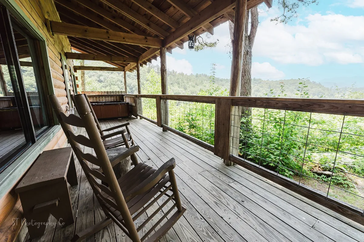 This image showcases a covered deck with classic wooden rocking chairs facing tranquil greenery, framed by a wooden railing. The setting suggests a peaceful retreat directly connected to the natural surroundings, ideal for relaxing after outdoor adventures.