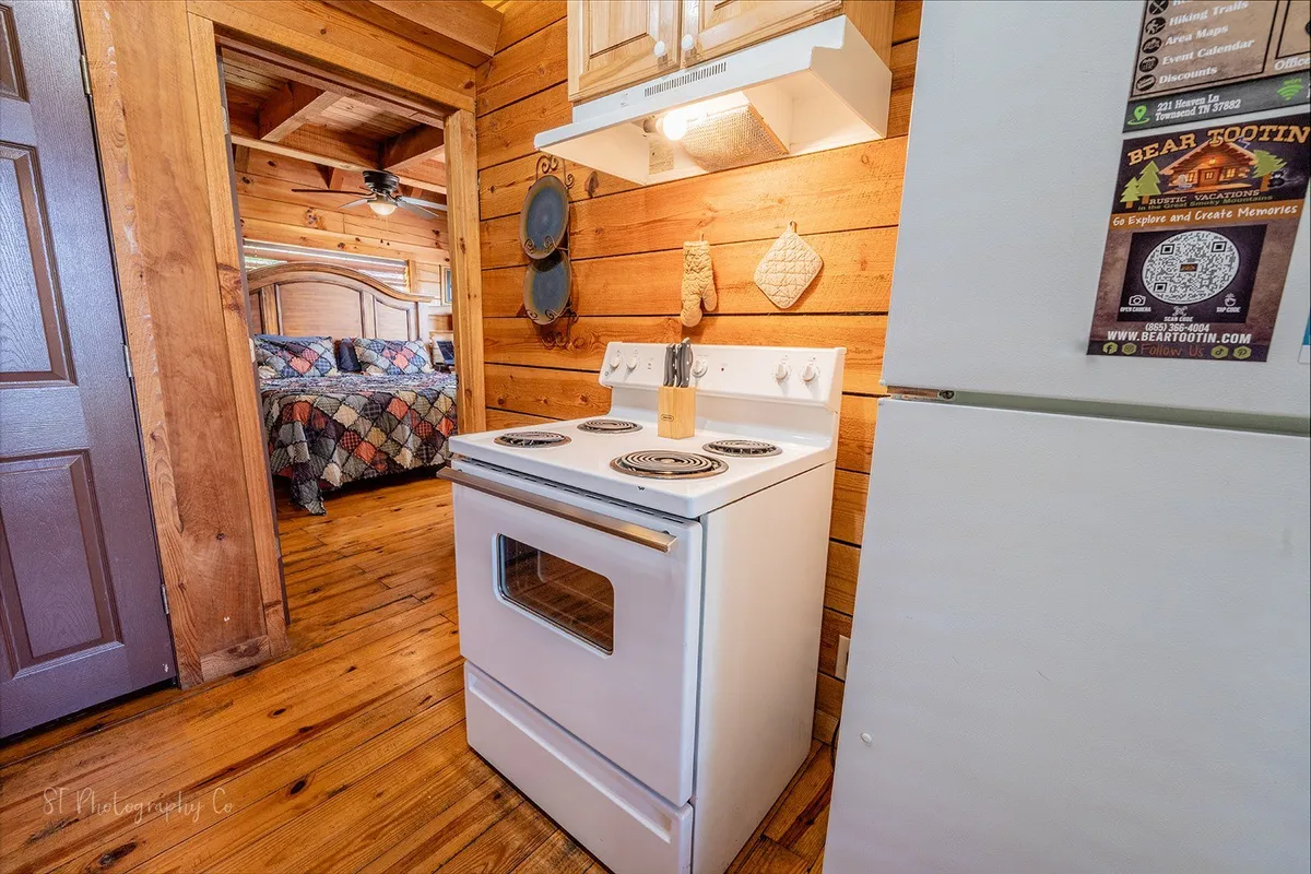 A bright, inviting kitchen with a white stove, wooden cabinets, and charming cabin decor. The atmosphere is warm and bustling, ideal for preparing family dinners or sharing holiday meals after a day spent exploring the Smokies.